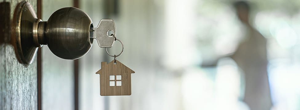 Out-of-province Agents Need a Licence to Trade in Alberta A key with a house-shaped keychain in a door lock, symbolizing homeownership and the excitement of securing a new home.