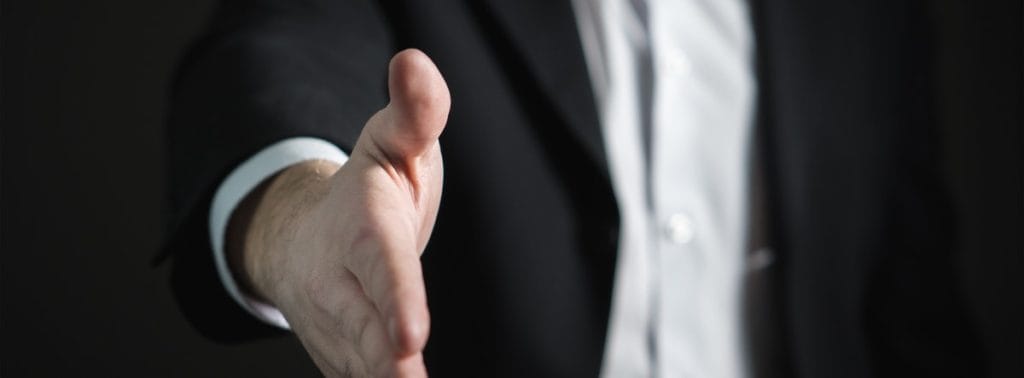 Unlicensed Activity A businessman in a suit extending his hand for a handshake, symbolizing professionalism, trust, and welcoming service in real estate or business interactions.